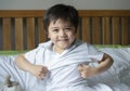 School boy sitting in bed and try to wearing his cloth with smiling face,Cute kid boy getting dressed and get ready for school, Royalty Free Stock Photo