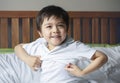 School boy sitting in bed and try to wearing his cloth with smiling face,Cute kid boy getting dressed and get ready for school, Royalty Free Stock Photo