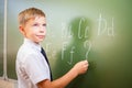 School boy writes English alphabet with chalk on blackboard