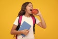 School child, teenage student girl with bagpack hold apple and book isolated on yellow. Amazed teen girl. Excited