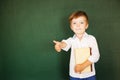 School child thumbs up and hold book over blackboard. Free text, copy space Royalty Free Stock Photo