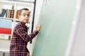 School child writing blackboard look at camera