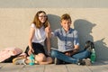 School children teens sit on gray wall, read textbooks, drink water, look at textbook. Boy looking at book and pointing forefinger