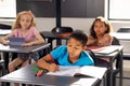 In school, in classroom, boy in blue shirt writing in notebook, two girls watching Royalty Free Stock Photo