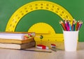 School concept: colore pencil, book, ruler, scissors and green chalkboard with yellow protractor.