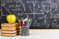 School desk in classroom, with books on background of chalk board with written formulas. Soncept Teacher`s Day