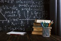 School desk in classroom, with books on background of chalk board with written formulas. Soncept Teacher`s Day