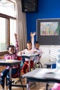 In school, diverse children raising hands in classroom, participating in lesson Royalty Free Stock Photo