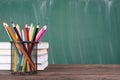 School education concept. Close-up photo of colorful crayons and stack of textbooks isolated on green chalkboard copyspace