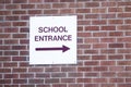 School entrance direction arrow sign on brick wall