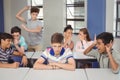 School friends bullying a sad boy in classroom