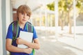 School-age boy holding tablet while standing on school walkway wearing blue polo shirt and backpack Royalty Free Stock Photo