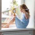 School girl combs her hair sitting on the windowsill, rainy weather outside