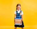 School girl holding heavy textbooks on yellow studio background Royalty Free Stock Photo