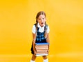 School girl holding heavy textbooks on yellow studio background Royalty Free Stock Photo