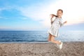 School girl jumping on beach near sea, space for text. Summer holidays Royalty Free Stock Photo