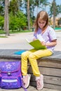 School girl sitting on the bench in public park and making notes to note book