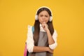 School girl, teenager student in headphones on yellow isolated studio background. Music school concept. Thinking face Royalty Free Stock Photo