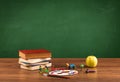 School items on desk with empty chalkboard Royalty Free Stock Photo