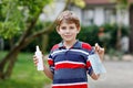 School kid boy with medical mask as protection against pandemic coronavirus quarantine disease. Child holding bottle Royalty Free Stock Photo