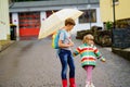 School kid boy picks up the little sister, preschool girl from kindergarten. Two happy children with umbrella playing