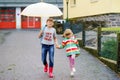 School kid boy picks up the little sister, preschool girl from kindergarten. Two happy children with umbrella playing