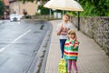 School kid boy picks up the little sister, preschool girl from kindergarten. Two happy children with umbrella playing