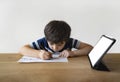 School Kid using pen drawing on paper, A boy doing home work sitting with mock up tablet, Child using digital pad searching Royalty Free Stock Photo