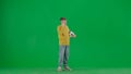 Portrait of kid boy on chroma key green screen. Schoolboy in jeans holding football ball and talking on smartphone. Full