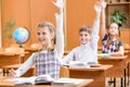 School kids with raised hands at lesson in classroom Royalty Free Stock Photo