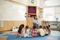 School kids sitting on the floor gathered around teacher