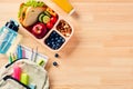 School lunch box with sandwich, fruits, vegetables, bottle of water, and kids backpack with school supplies on wooden table. Flat Royalty Free Stock Photo