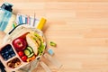 School lunch box with sandwich, vegetables, bottle of water, almonds and fruits and backpack with school supplies on wooden desk Royalty Free Stock Photo