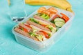 School lunch box with sandwich, vegetables, water, and fruits on table.