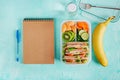 School lunch box with sandwich, vegetables, water, and fruits on table.