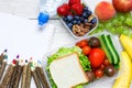 School lunch boxes with sandwich, fruits, vegetables and bottle of water with colored pencils