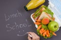 School meals. Lunch box with a sandwich, fresh vegetables and fruits, a bottle of juice on a dark background. Chalk writing Lunch Royalty Free Stock Photo