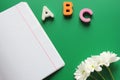 School notebook next to the letters ABC and white chrysanthemums on a green background