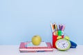 School and office supplies with green apple and alarm clock on blue background, back to school Royalty Free Stock Photo