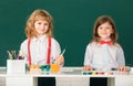 School smiling children girl and boy painting with paints color and brush in classroom on school blackboard background