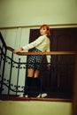 On the school staircase, a ginger Asian schoolgirl stand in uniform, holding onto the handrail. Strength of a young student