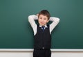 School student boy posing at the clean blackboard, grimacing and emotions, dressed in a black suit, education concept, studio Royalty Free Stock Photo