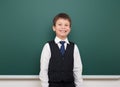 School student boy posing at the clean blackboard, grimacing and emotions, dressed in a black suit, education concept, studio Royalty Free Stock Photo