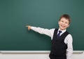 School student boy posing at the clean blackboard, show finger and point at, grimacing and emotions, dressed in a black suit, educ Royalty Free Stock Photo