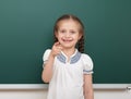 School student girl posing at the clean blackboard, grimacing and emotions, dressed in a black suit, education concept, studio pho Royalty Free Stock Photo