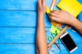 school students hand cleans away the school supplies on blue wooden table background. student prefers to perform other tasks.