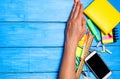 school students hand cleans away the school supplies on blue wooden table background. student prefers to perform other tasks.