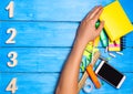 school students hand cleans away the school supplies on blue wooden table background. student prefers to perform other tasks.