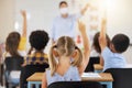 School students raising hands to volunteer, participate and answer during lesson while learning in a classroom. Teacher