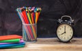 School supplies and alarm clock on wooden desk, blackboard background